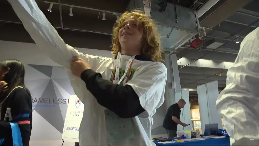 A student in a lab coat reaches upward during a hands-on Innovation Week activity.