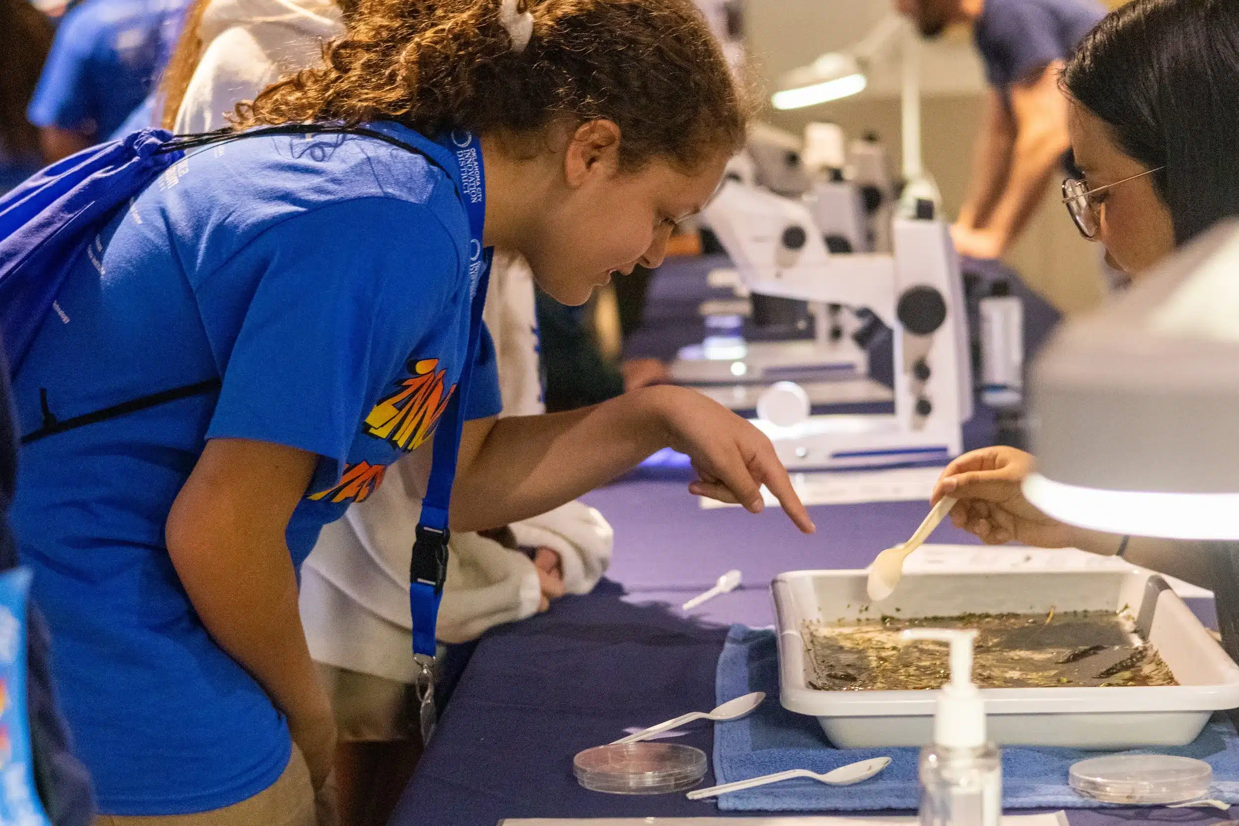 An OKCPS student examines a pond-water sample at a science activity table during Innovation Week.