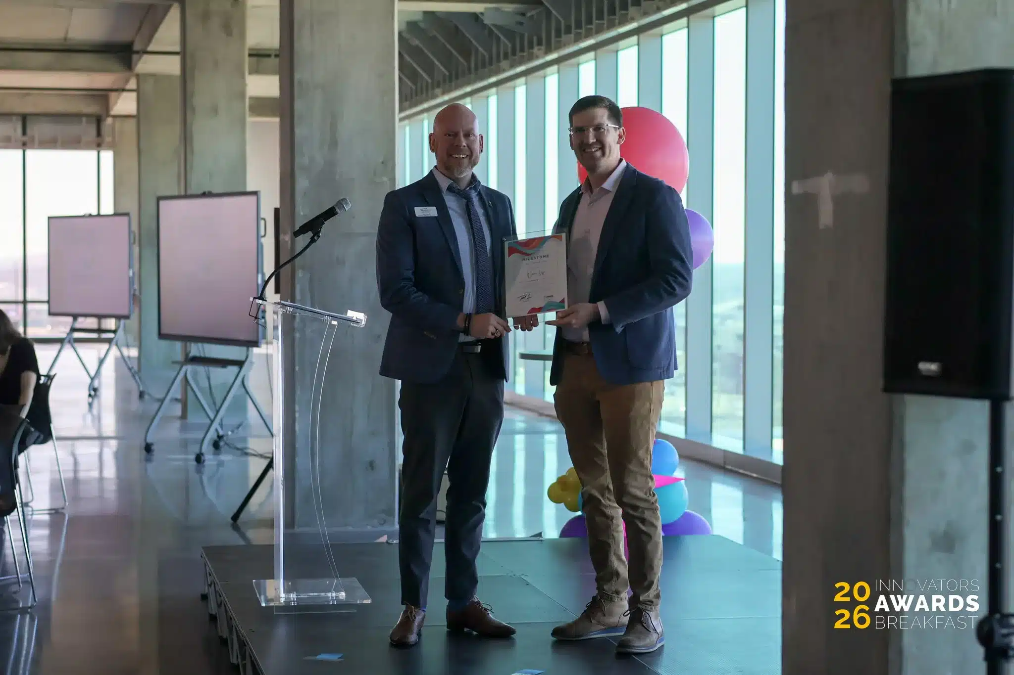 Two men hold an award together at the Innovators Awards Breakfast.