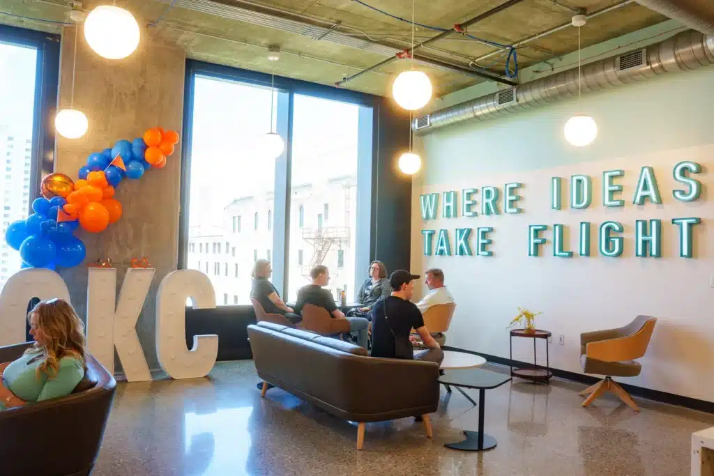 People gather in The Verge’s lounge beneath a wall sign reading “Where ideas take flight.”