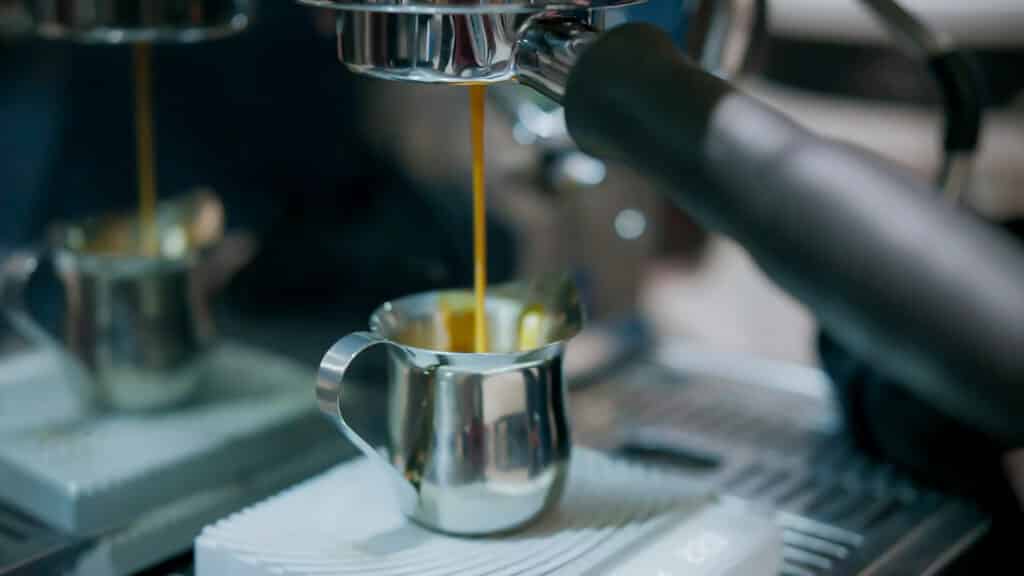 Espresso pours from a coffee machine into a small metal pitcher at Elemental Coffee.