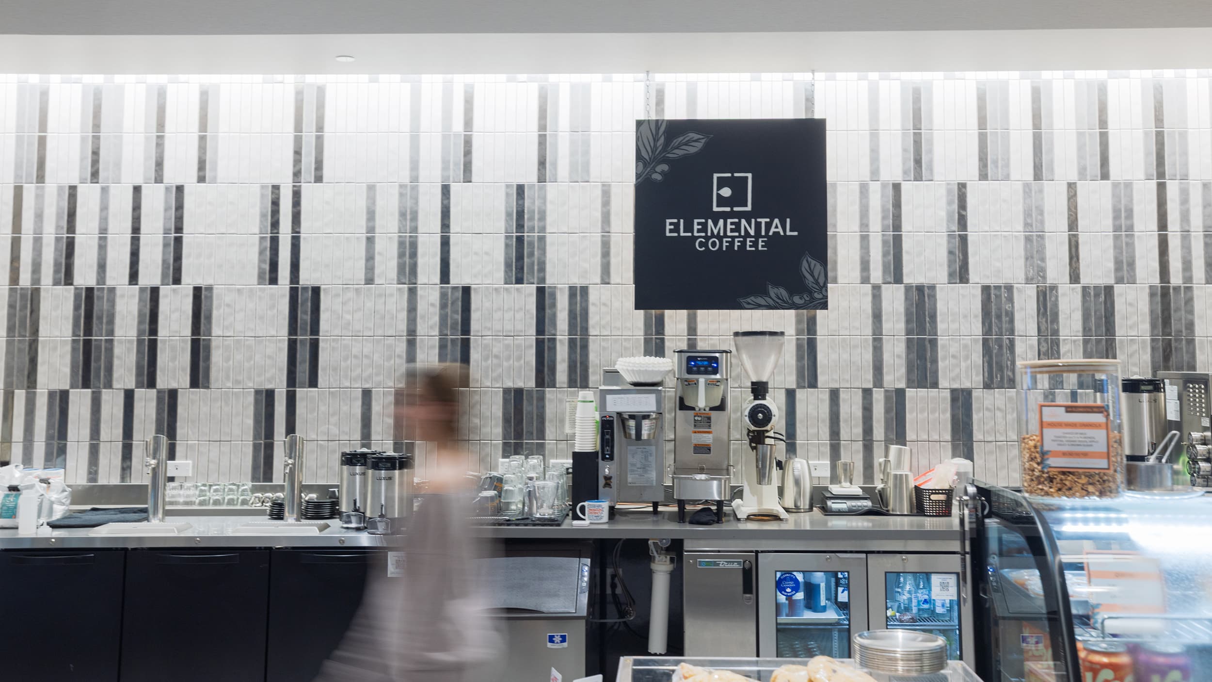 Elemental Coffee counter with espresso machines, a patterned tile wall, and a refrigerated display.