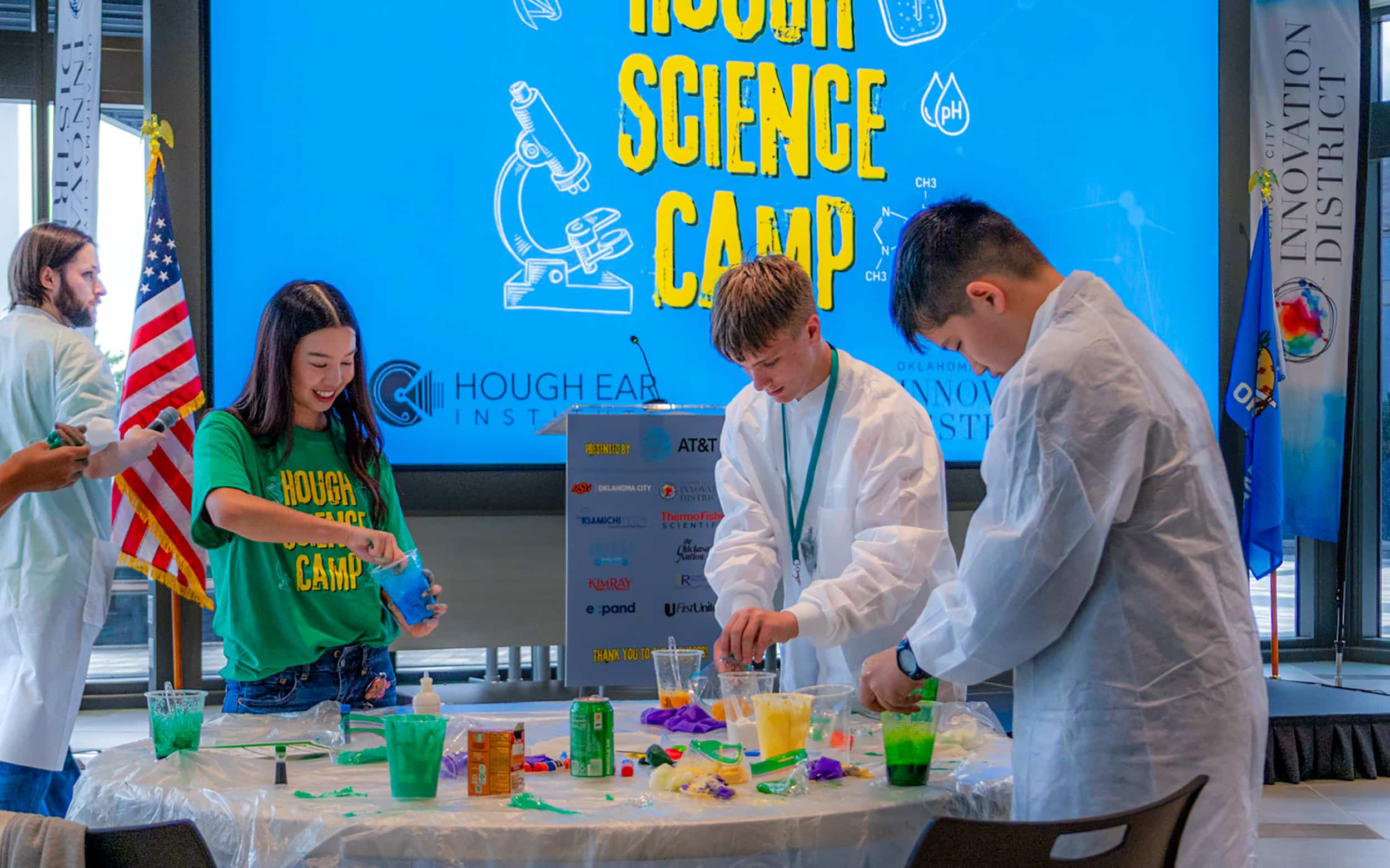 Children in lab coats take part in a colorful science activity at a Community Night demonstration table.