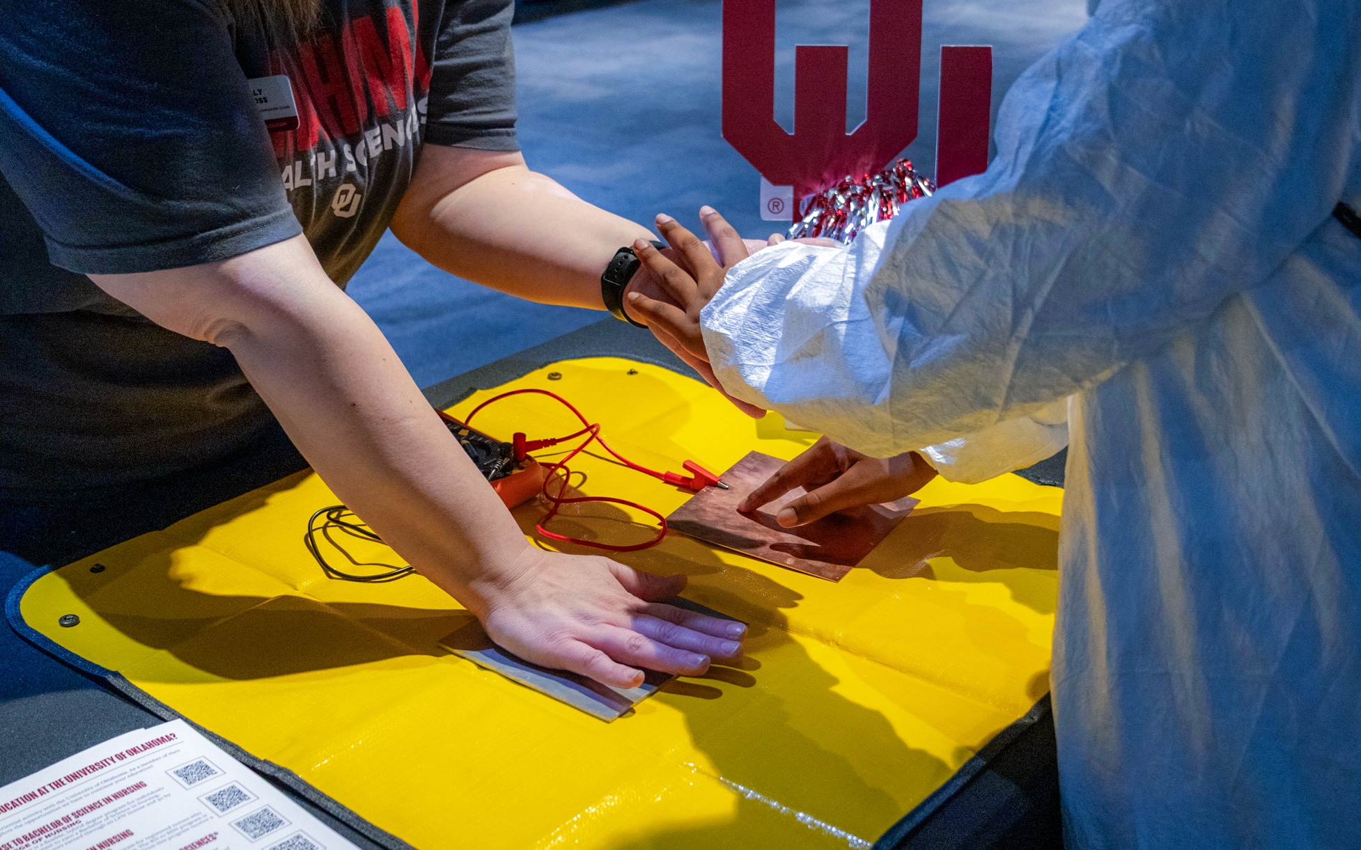 A student in a protective gown explores a hands-on medical demonstration with an instructor.