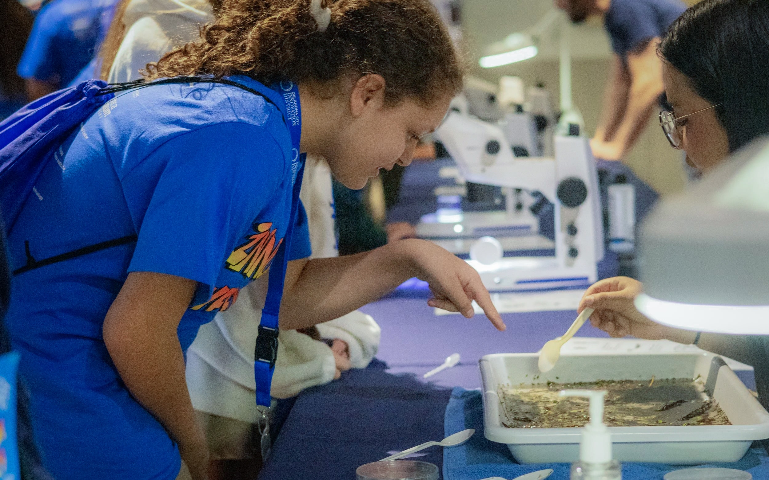 An OKCPS student examines a pond-water sample at a science activity table during Innovation Week.