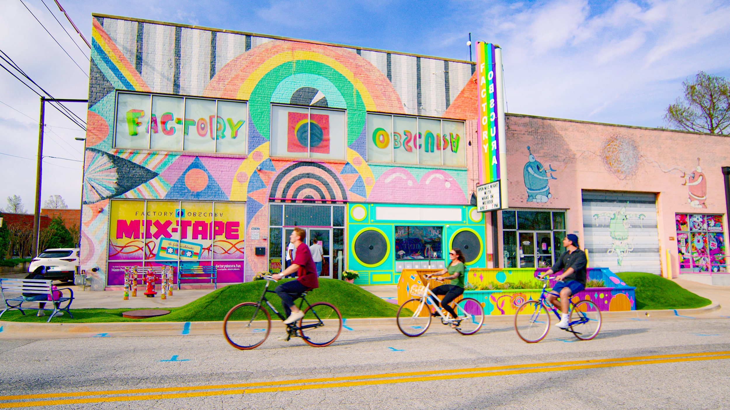 Cyclists ride past the colorful Factory Obscura MIX-TAPE mural.