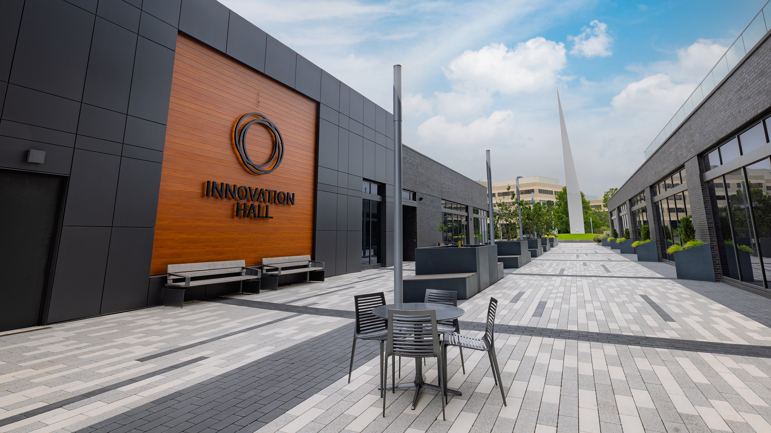Outdoor tables along Innovation Hall’s pedestrian plaza, with the Beacon of Hope sculpture in the distance.