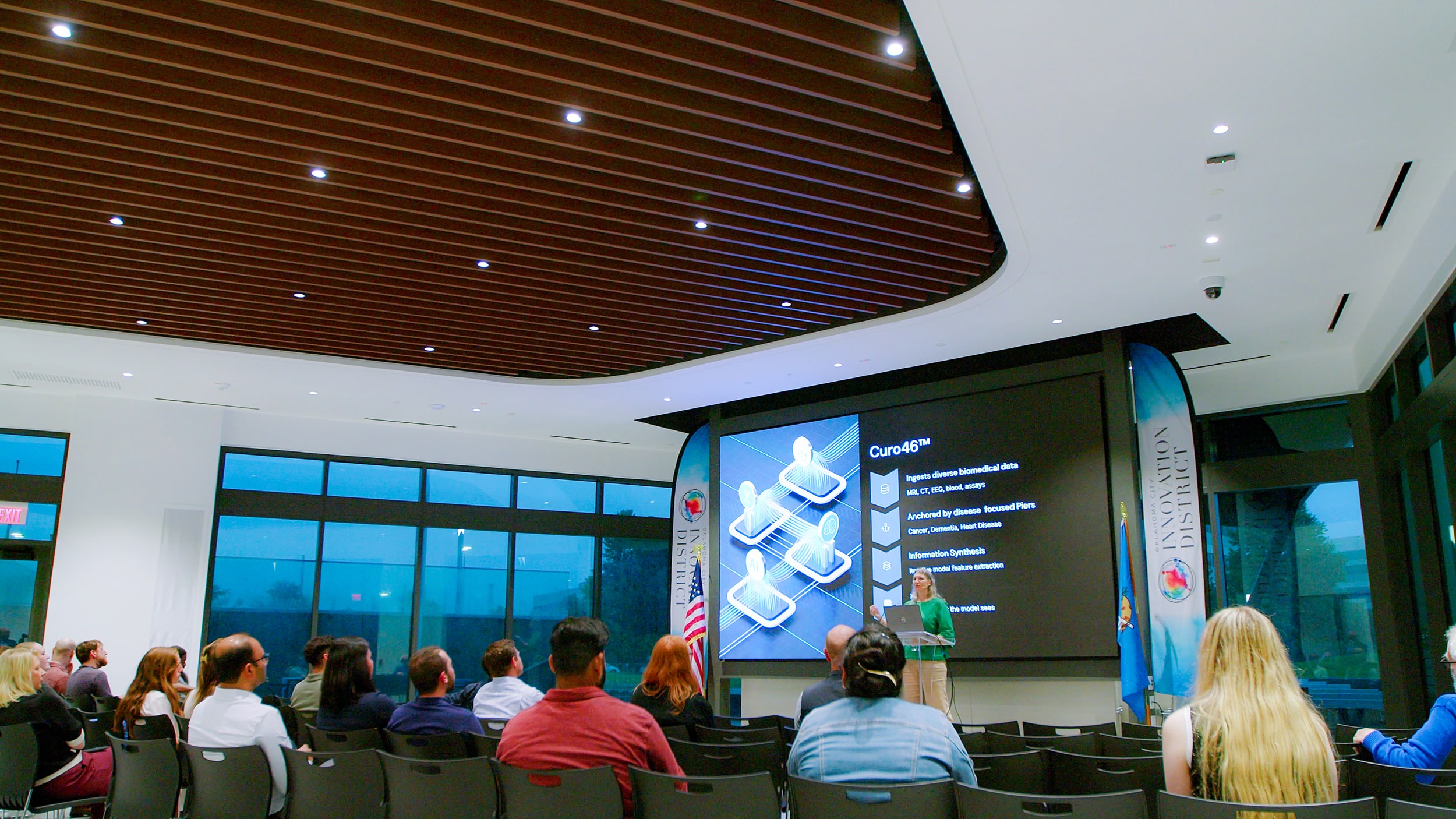 Guests attend a presentation in Innovation Hall’s auditorium beneath a curved wood-slat ceiling.