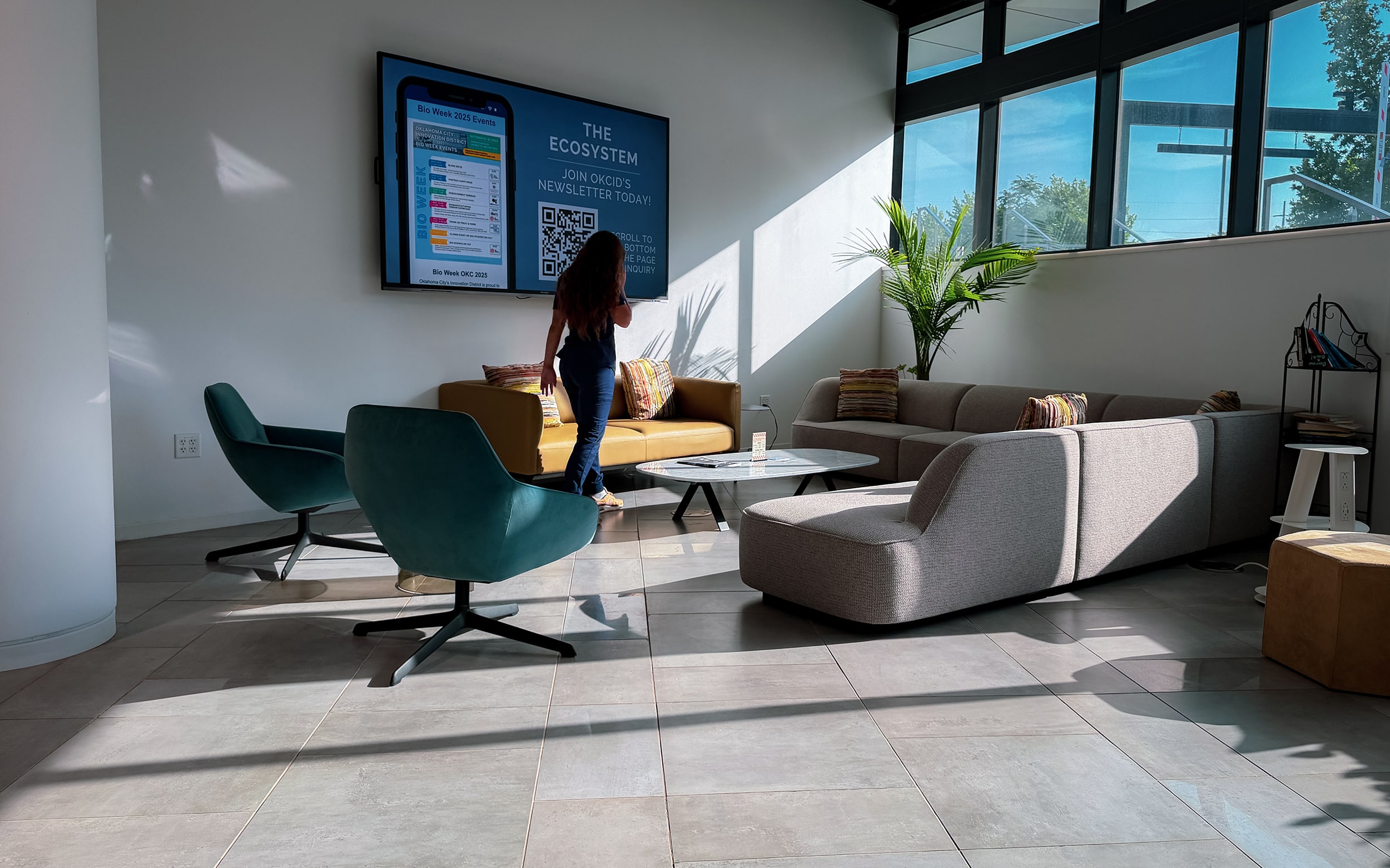 A visitor sits in a sunlit lounge area beside an information display at Innovation Hall.